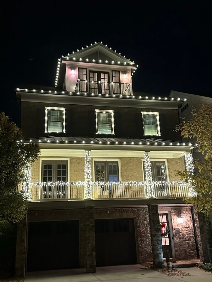 A three-storey brick townhouse at night — roofline, window frames, porch columns and railings all outlined in crisp white light