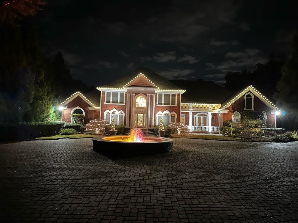 A columned brick estate at night with a warm white roofline, spiral-wrapped porch columns and a fountain in the circular drive